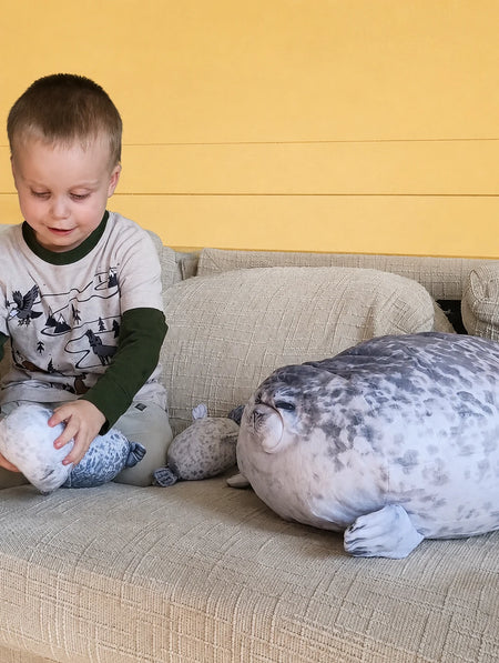 Child playing with three seal stuffed animals on a living room sofa