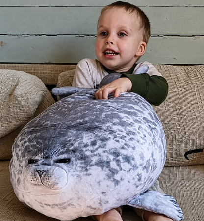 SQEQE seal stuffed animal with babies hugged by a child under warm bedroom lighting